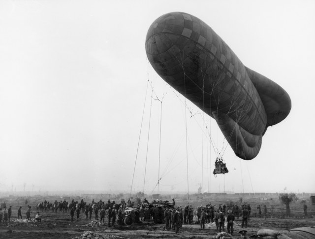 Een kabelballon stijgt op bij Ieper met twee waarnemers in de mand, terwijl soldaten de touwen vasthouden.